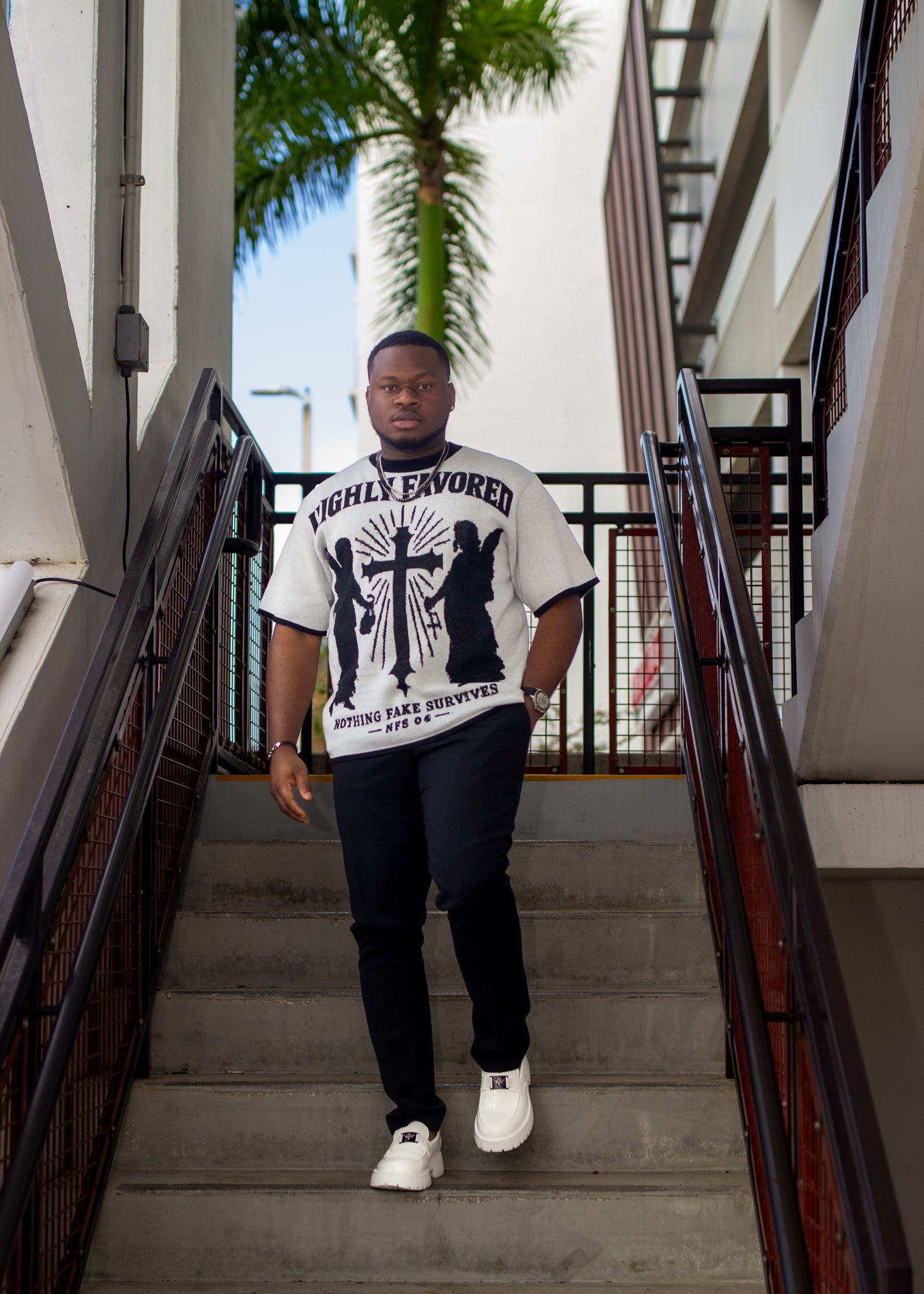 Man standing on a staircase wearing a graphic t-shirt with text and images.