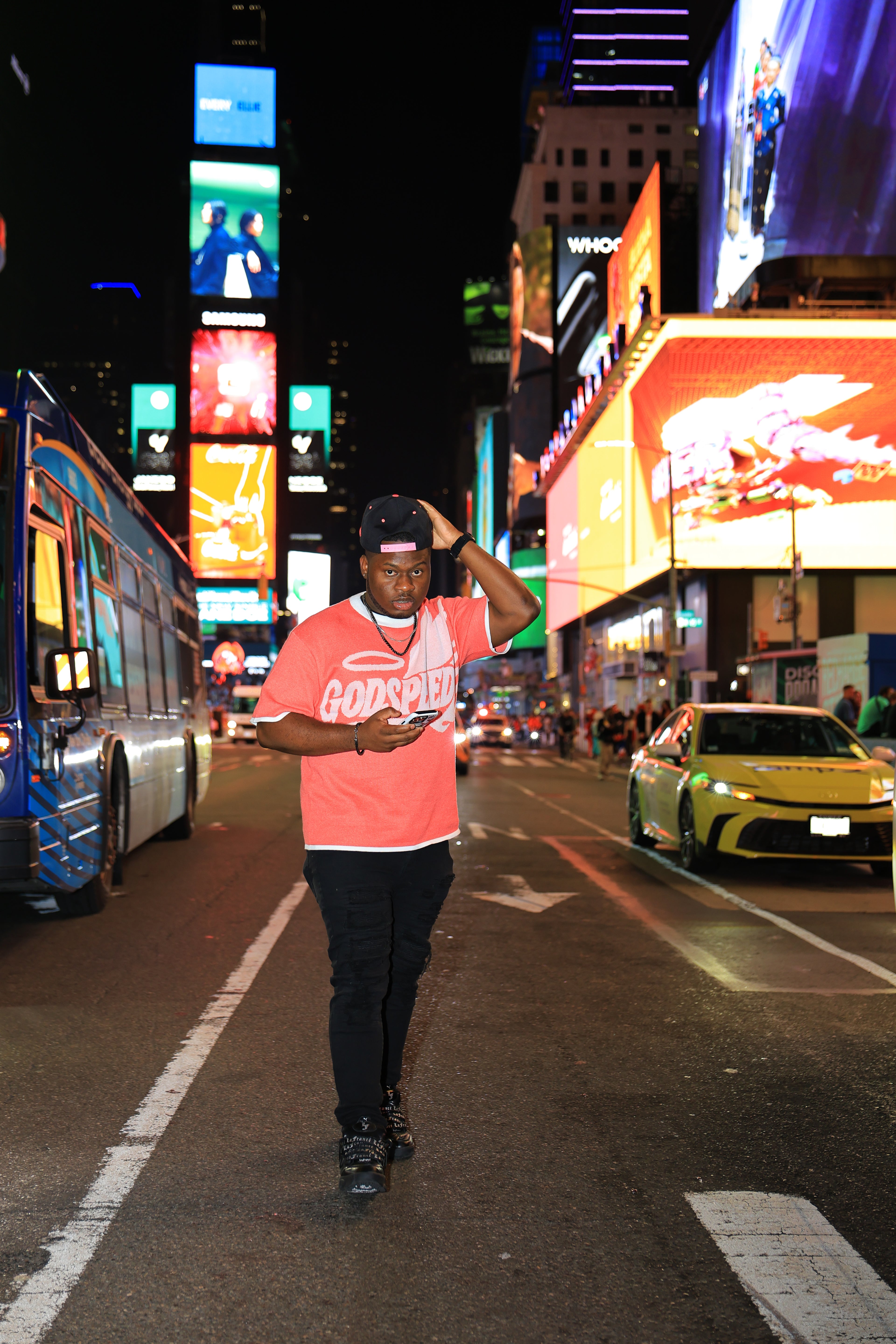 Person walking on a busy street at night with illuminated billboards and vehicles.