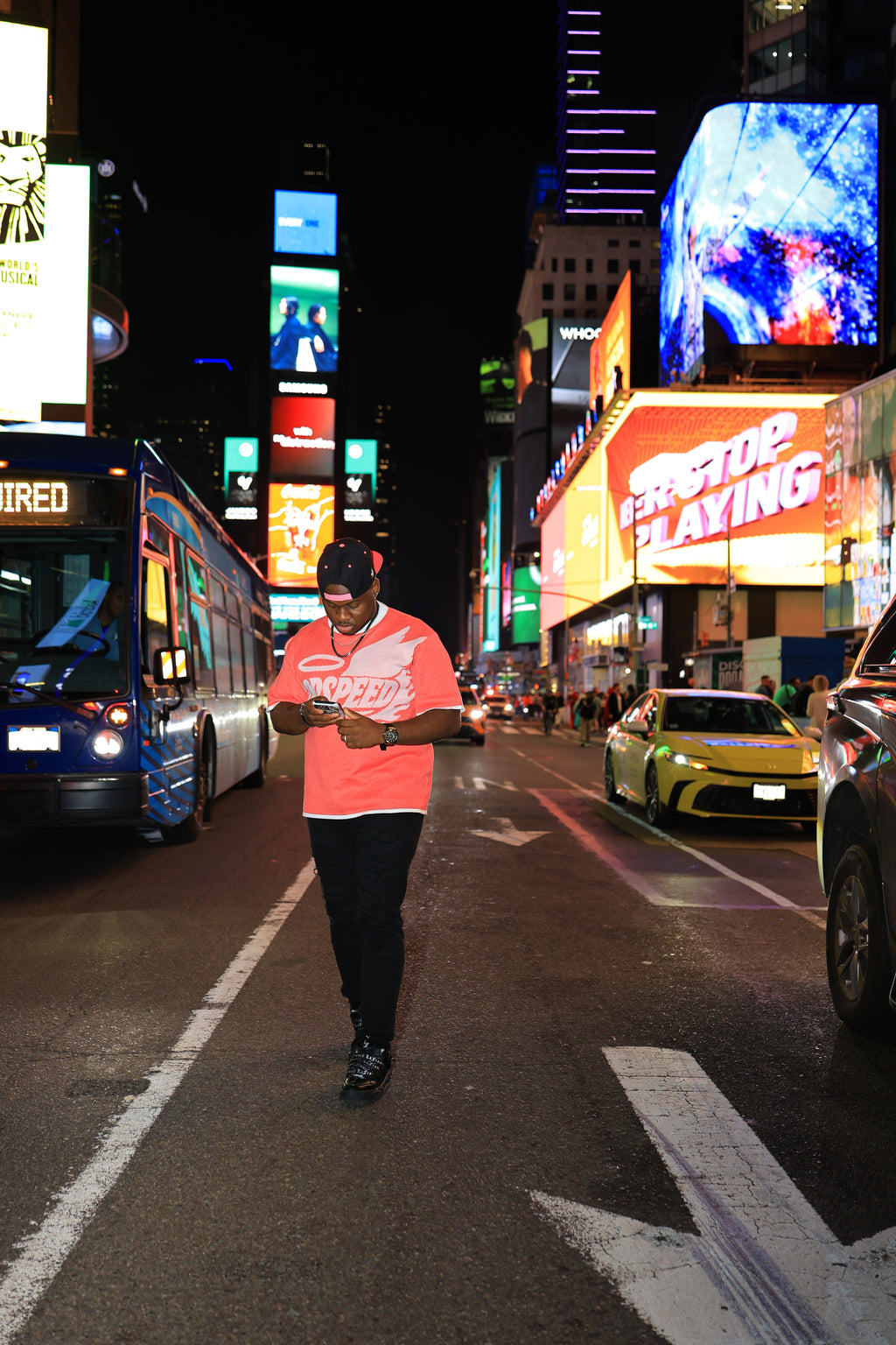 Person walking on a busy city street at night with illuminated billboards and vehicles.