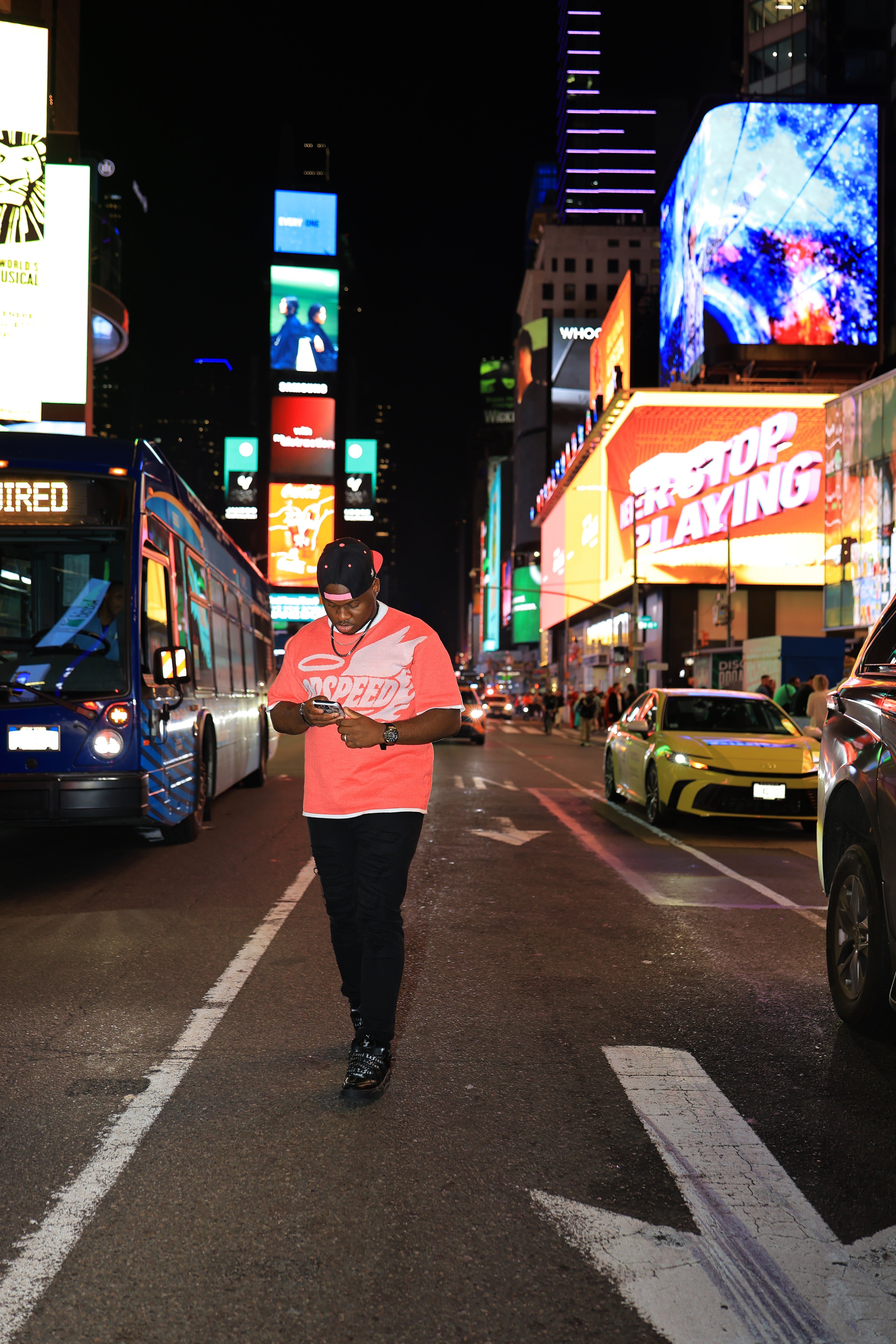 Person walking on a busy city street at night with illuminated billboards and vehicles.
