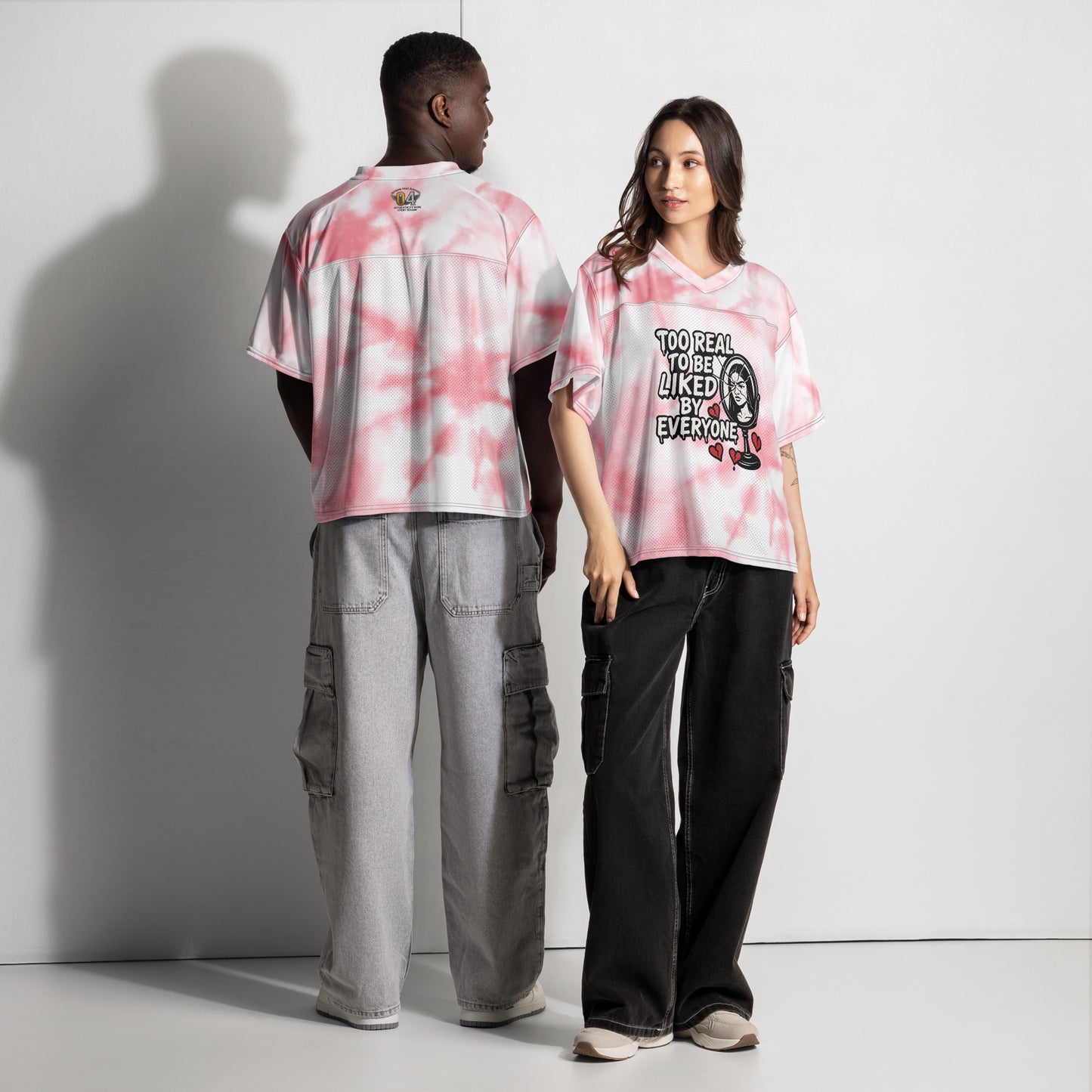 Two people wearing pink and white tie-dye shirts with graphic designs on a plain background