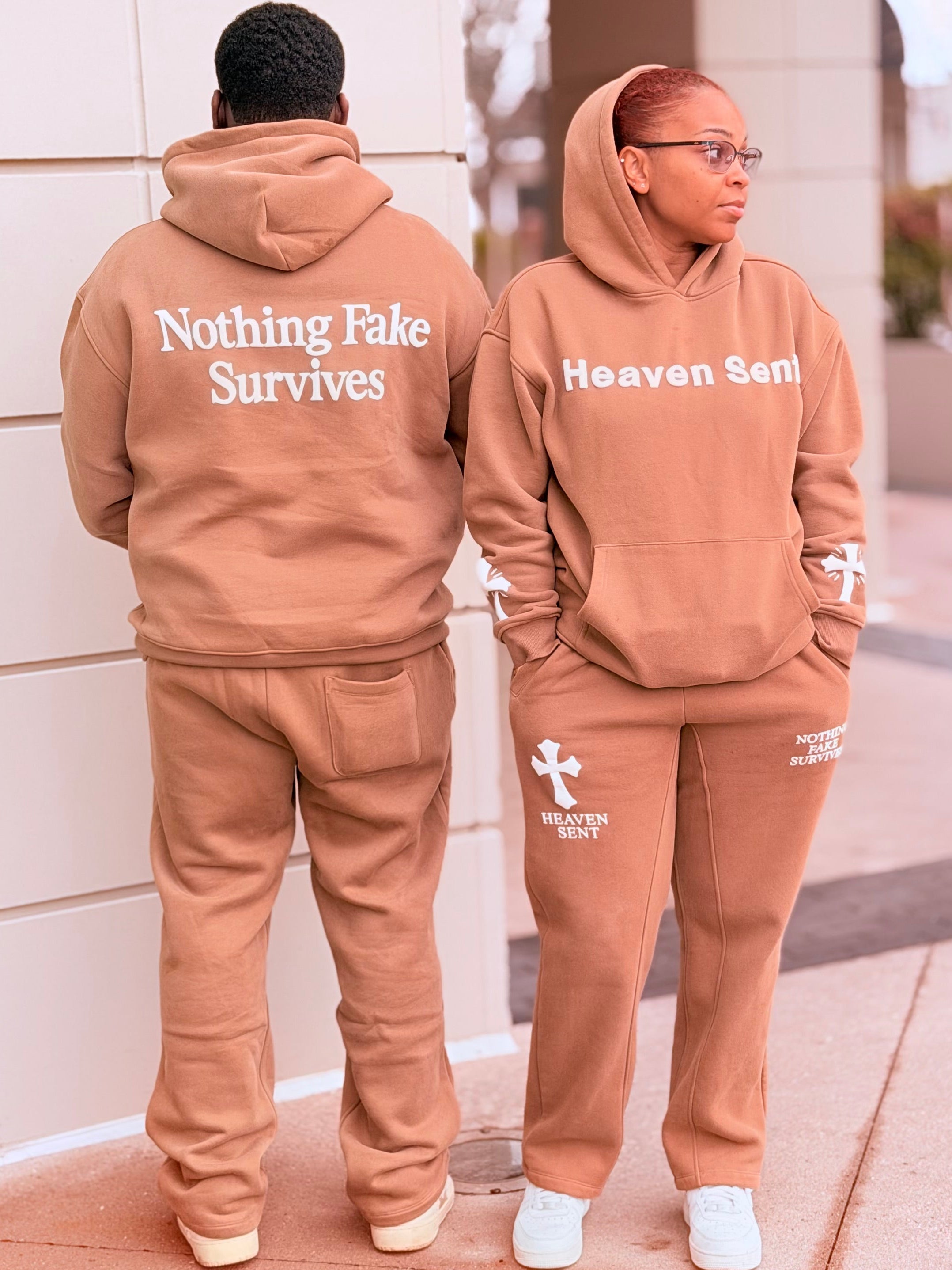 Two people wearing matching brown hoodies and pants with text on a city street.